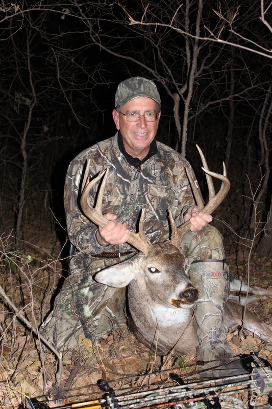Dale Sader in camouflage with recently killed buck in the wild with a bow nearby